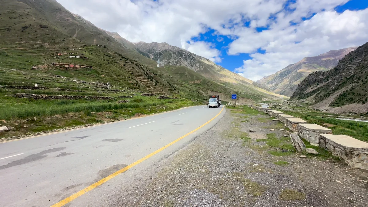Ameera parked beside a mountain road beneath green slopes and clouds