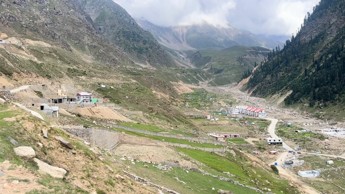 A broad view down a mountain valley with a river, pine slopes and a winding road